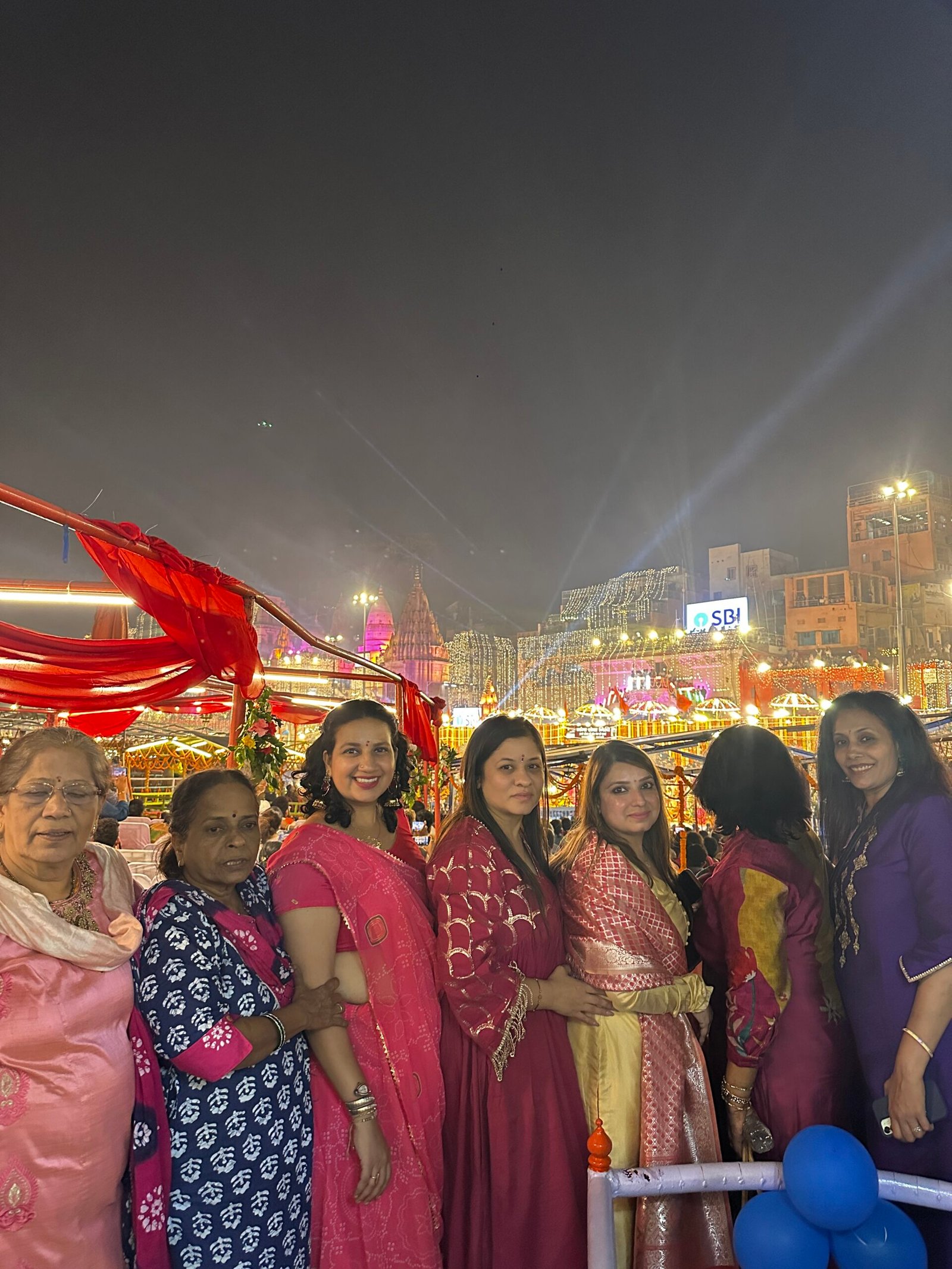 Guests on a decorated boat with illuminated Varanasi ghats behind them during Dev Deepawali 2025
