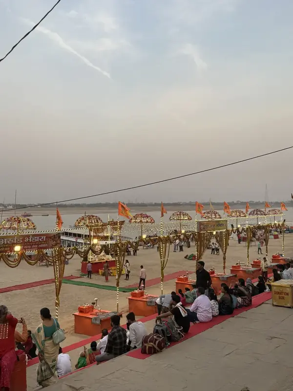 Visitors seated by orange aarti platforms on a Varanasi ghat before the evening Ganga Aarti