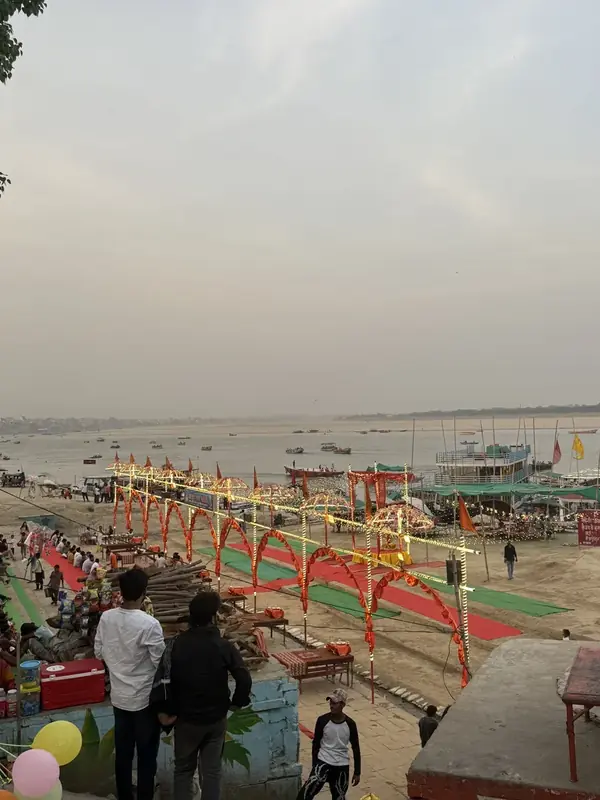 Wide view of a Varanasi ghat with red arches, aarti platforms and boats on the Ganga in daylight