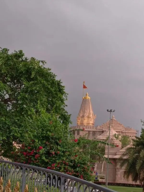 Spire and saffron flag of Shri Ram Janmabhoomi Mandir in Ayodhya seen through trees under a cloudy sky